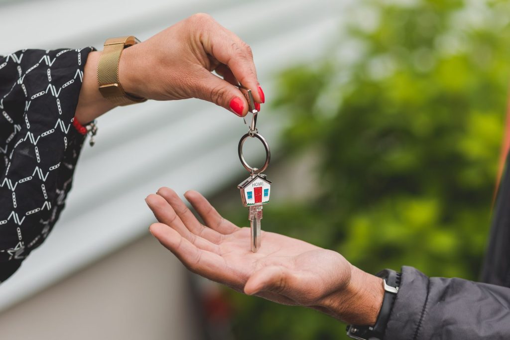 Eine Hand übergibt einen Wohnungsschlüssel mit Haus-Anhänger an eine andere Hand